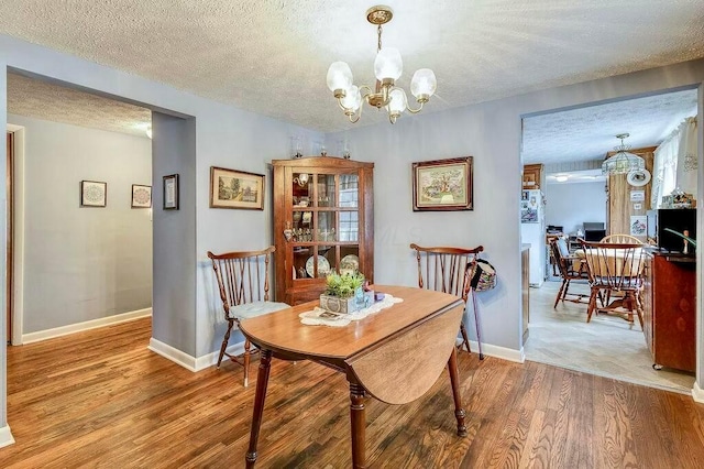 dining space featuring a textured ceiling, wood finished floors, baseboards, and a chandelier