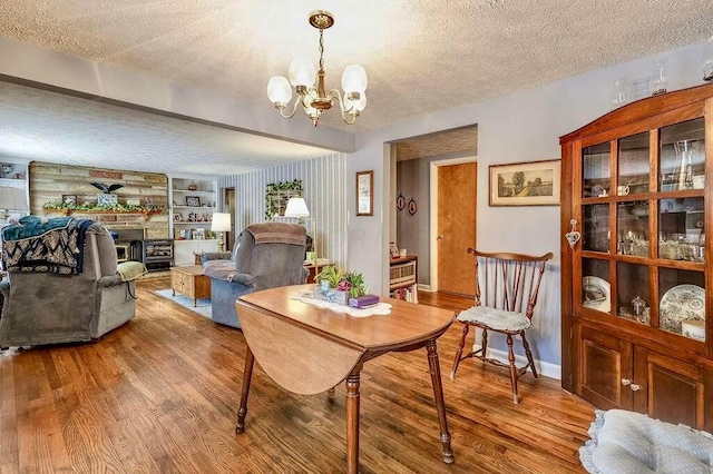 dining space with a textured ceiling, wood finished floors, a stone fireplace, an inviting chandelier, and baseboards