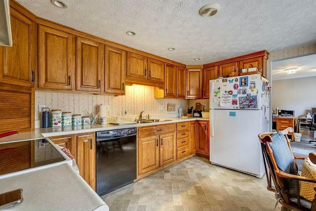 kitchen featuring dishwasher, light countertops, freestanding refrigerator, brown cabinetry, and a sink