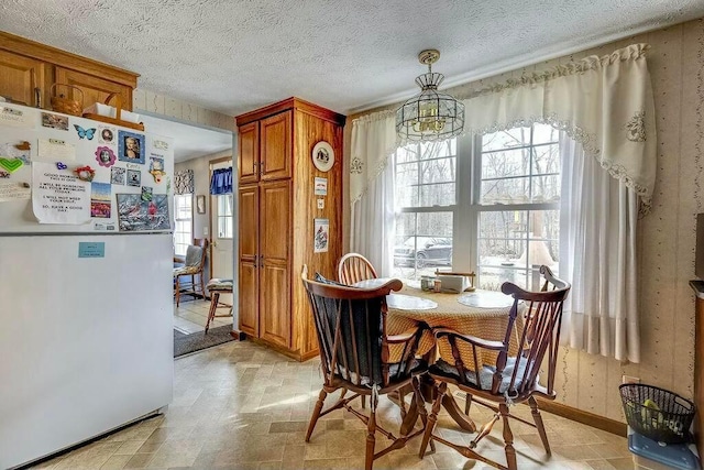 dining area with baseboards, a textured ceiling, a healthy amount of sunlight, and stone finish floor