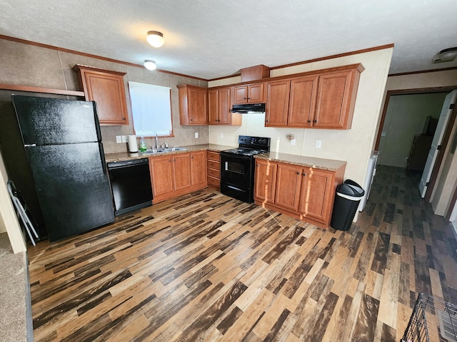 kitchen featuring black appliances, a sink, wood finished floors, brown cabinetry, and crown molding