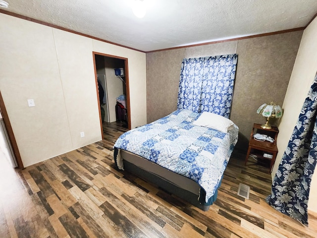 bedroom with wood finished floors, visible vents, ornamental molding, a textured ceiling, and a walk in closet