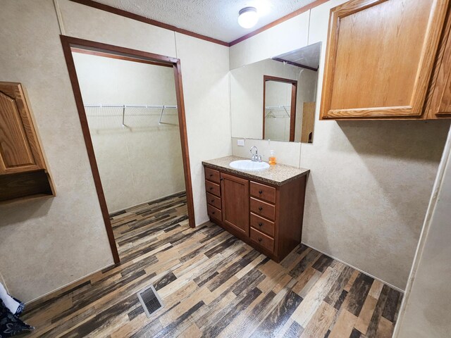 bathroom with a walk in closet, ornamental molding, a textured ceiling, wood finished floors, and vanity