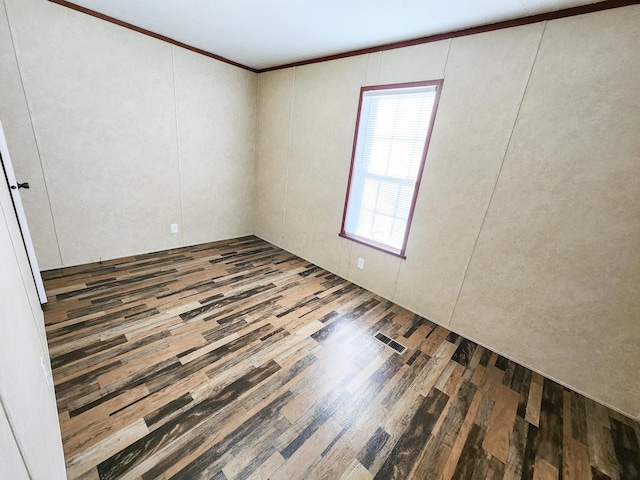 unfurnished room featuring visible vents, wood finished floors, and ornamental molding