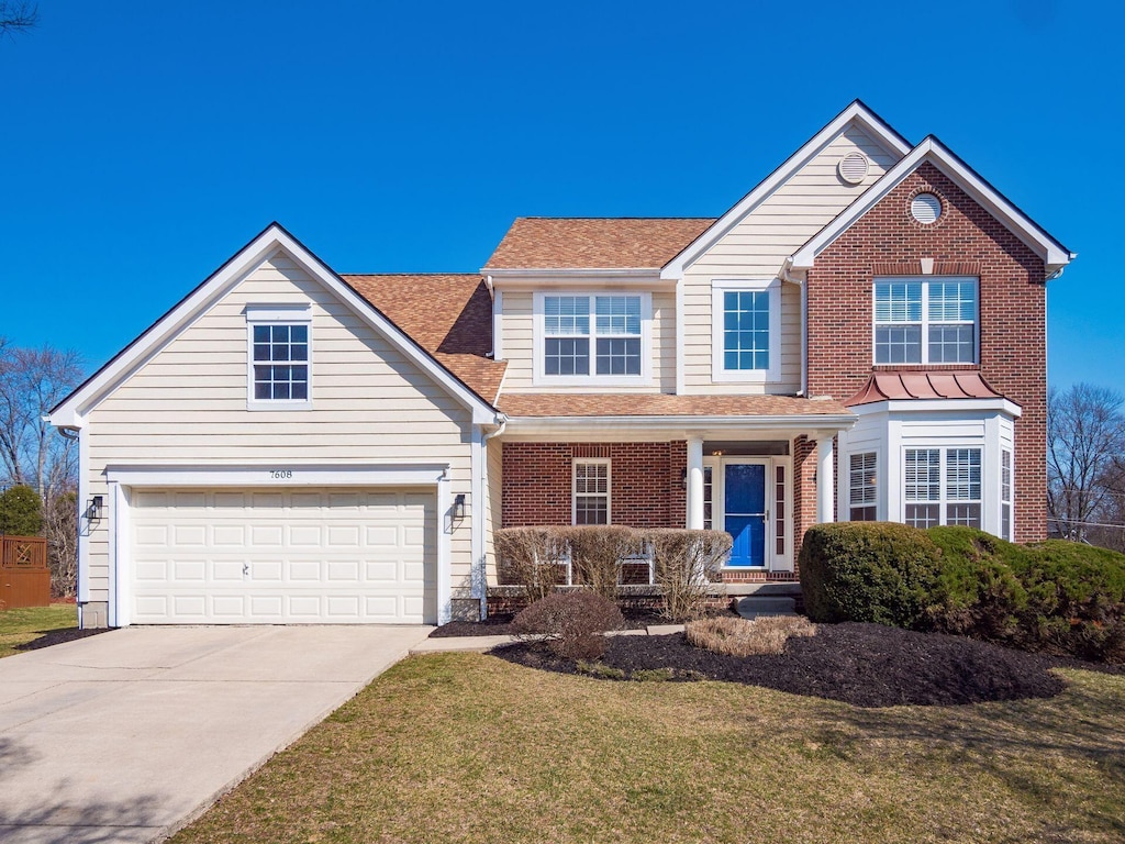 traditional home with a front yard, roof with shingles, concrete driveway, a garage, and brick siding