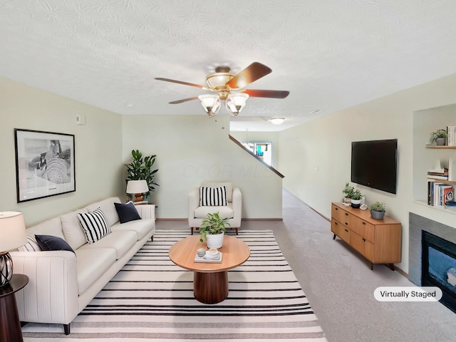 carpeted living room with ceiling fan, baseboards, and a textured ceiling