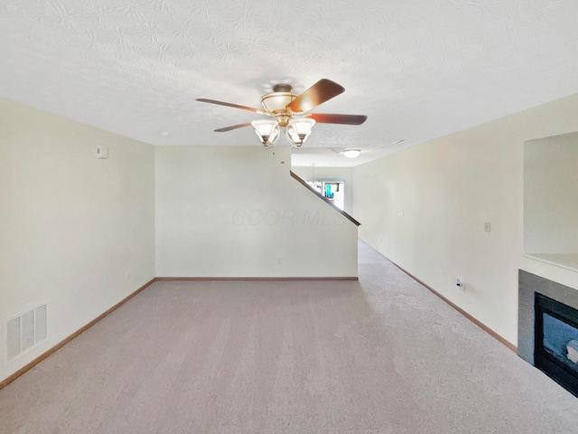 unfurnished living room with visible vents, carpet, a glass covered fireplace, a textured ceiling, and a ceiling fan