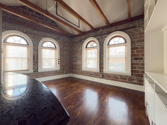 interior space featuring plenty of natural light, brick wall, dark wood-type flooring, and lofted ceiling with beams