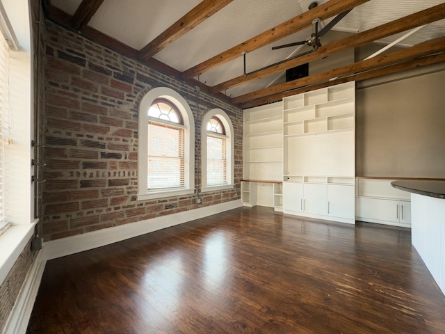 unfurnished room with a ceiling fan, beamed ceiling, wood finished floors, and brick wall