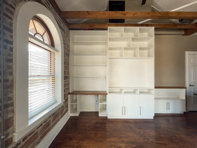 spare room featuring beamed ceiling, a healthy amount of sunlight, brick wall, and wood finished floors