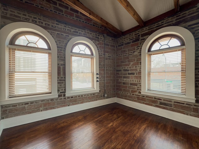 spare room featuring dark wood finished floors, lofted ceiling with beams, baseboards, and brick wall