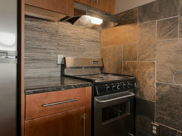 kitchen with dark countertops, tasteful backsplash, under cabinet range hood, electric stove, and brown cabinetry