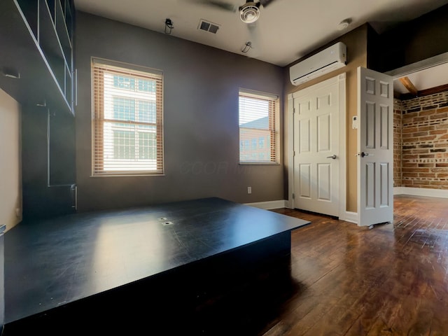 interior space featuring baseboards, brick wall, a wall mounted AC, ceiling fan, and dark wood-type flooring