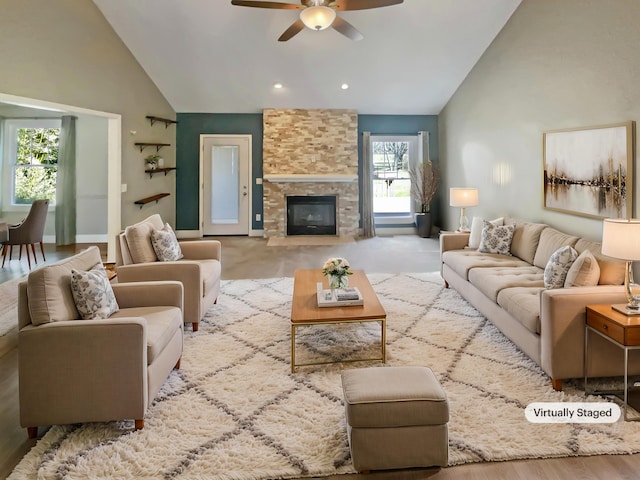 living area with a stone fireplace, a ceiling fan, and high vaulted ceiling