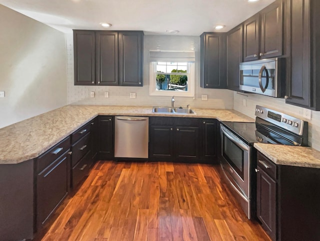 kitchen with dark wood finished floors, a peninsula, a sink, stainless steel appliances, and light countertops