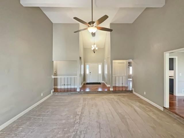 unfurnished living room with ceiling fan with notable chandelier, wood finished floors, baseboards, and high vaulted ceiling