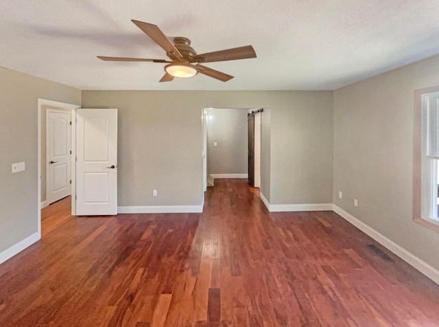 empty room featuring a barn door, wood finished floors, baseboards, and ceiling fan