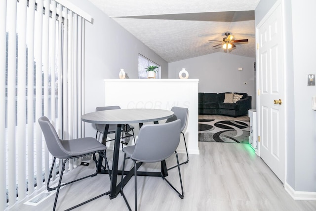 dining area featuring light wood finished floors, visible vents, vaulted ceiling, a textured ceiling, and a ceiling fan