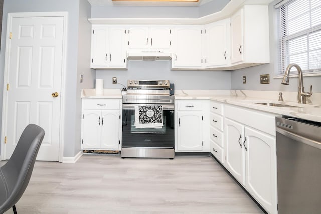 kitchen featuring light wood finished floors, a sink, stainless steel appliances, white cabinets, and under cabinet range hood