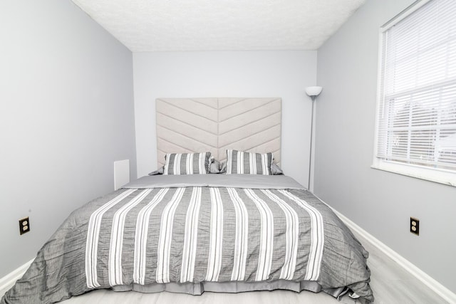 bedroom with a textured ceiling, baseboards, and wood finished floors