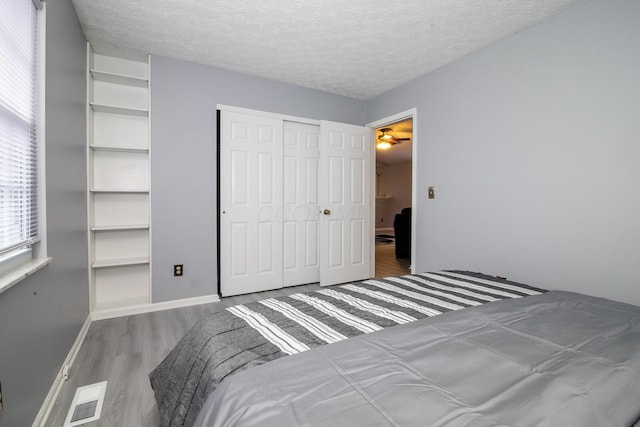 bedroom with a closet, visible vents, a textured ceiling, and wood finished floors