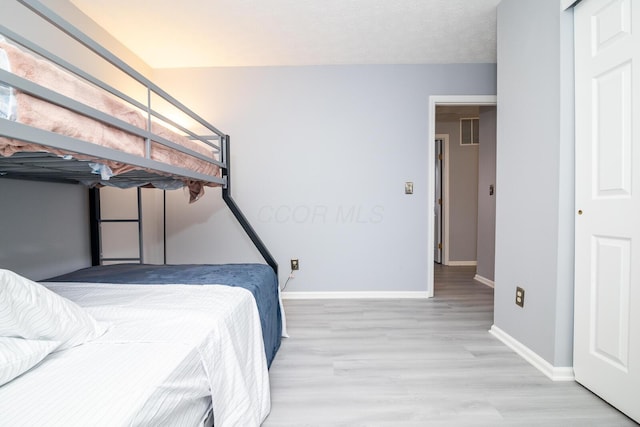 bedroom with light wood finished floors, visible vents, a textured ceiling, and baseboards