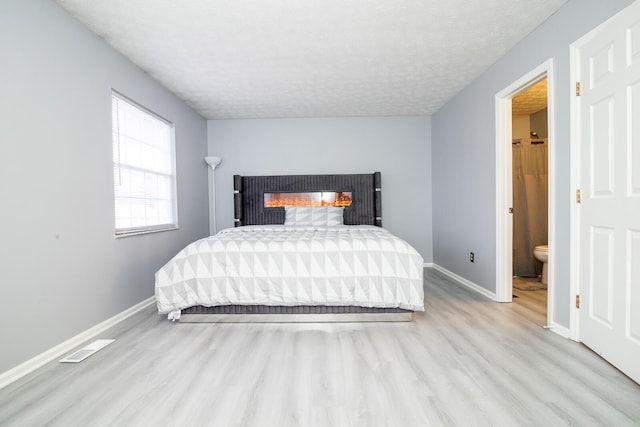 bedroom with a glass covered fireplace, a textured ceiling, baseboards, and wood finished floors