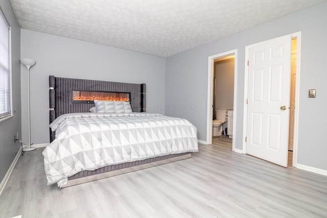 bedroom featuring a glass covered fireplace, baseboards, a textured ceiling, and wood finished floors