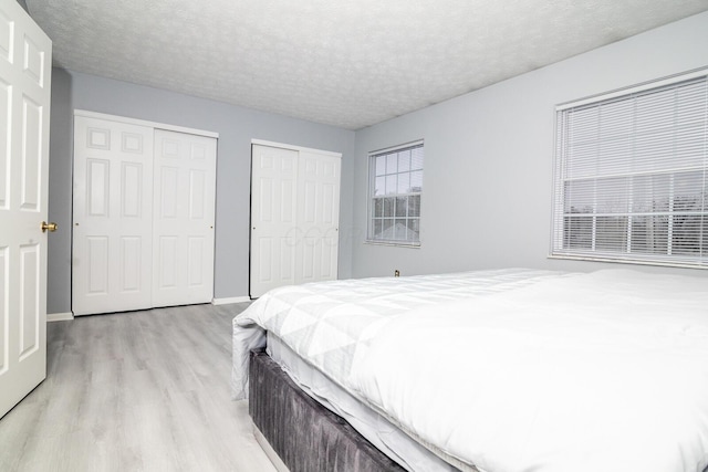 bedroom with light wood-style flooring, baseboards, multiple closets, and a textured ceiling