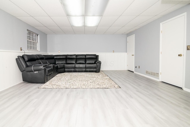 living room with a drop ceiling, visible vents, wood finished floors, and wainscoting