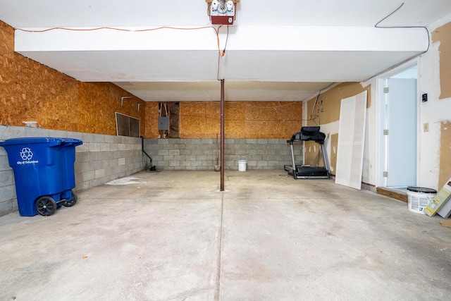 garage featuring electric panel, a garage door opener, and concrete block wall