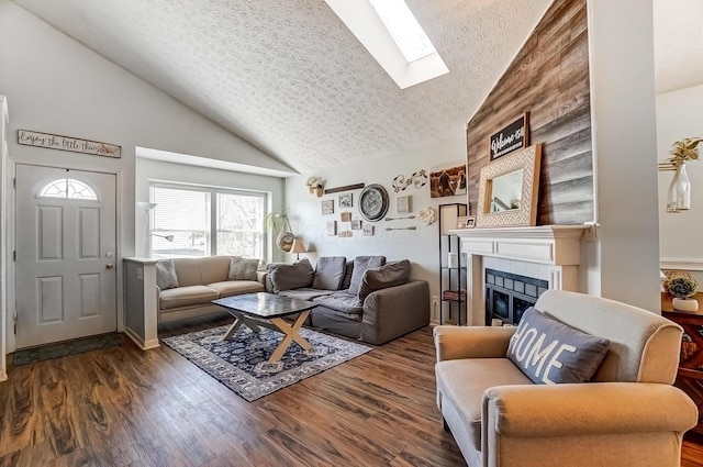 living area featuring high vaulted ceiling, a skylight, dark wood-style flooring, a tile fireplace, and a textured ceiling