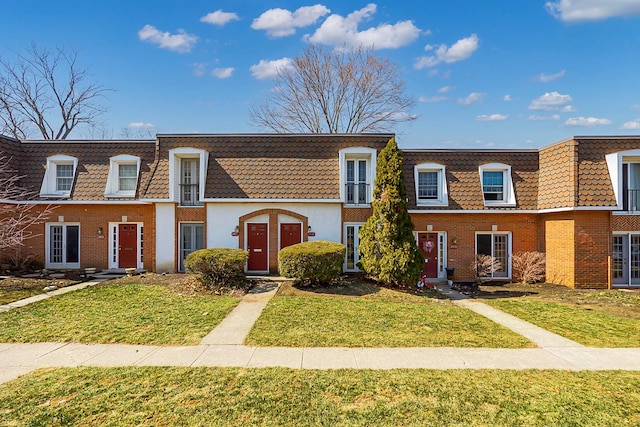 townhome / multi-family property with brick siding, mansard roof, and a front lawn