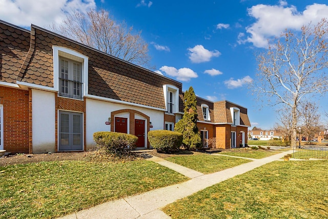 townhome / multi-family property featuring a front lawn, mansard roof, brick siding, and a residential view