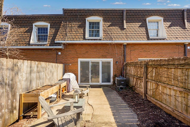 rear view of house with mansard roof, central AC, a fenced backyard, brick siding, and a patio area