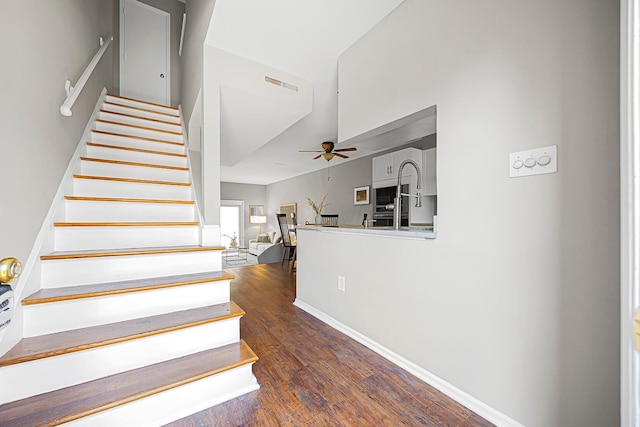 staircase featuring visible vents, lofted ceiling, a ceiling fan, wood finished floors, and baseboards