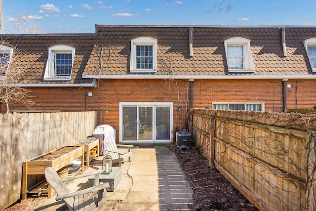 back of property with brick siding, a patio area, mansard roof, and fence