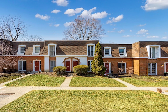 townhome / multi-family property featuring brick siding, mansard roof, and a front lawn