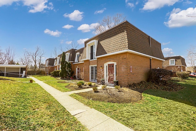 view of property exterior featuring fence, mansard roof, a shingled roof, a lawn, and brick siding