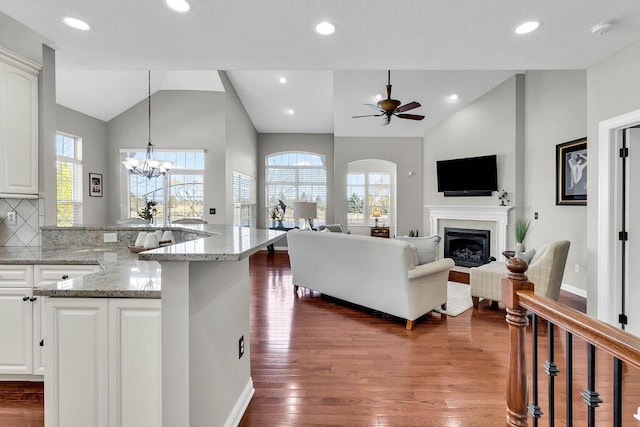 living area with wood finished floors, lofted ceiling, recessed lighting, a glass covered fireplace, and ceiling fan with notable chandelier