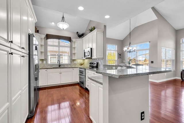 kitchen featuring a sink, open shelves, appliances with stainless steel finishes, a peninsula, and vaulted ceiling