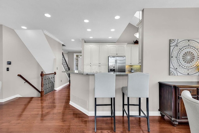 kitchen with white cabinetry, a peninsula, a breakfast bar area, stainless steel fridge with ice dispenser, and light stone countertops