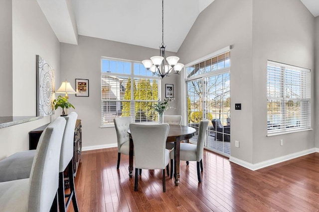 dining room featuring a notable chandelier, high vaulted ceiling, baseboards, and wood-type flooring