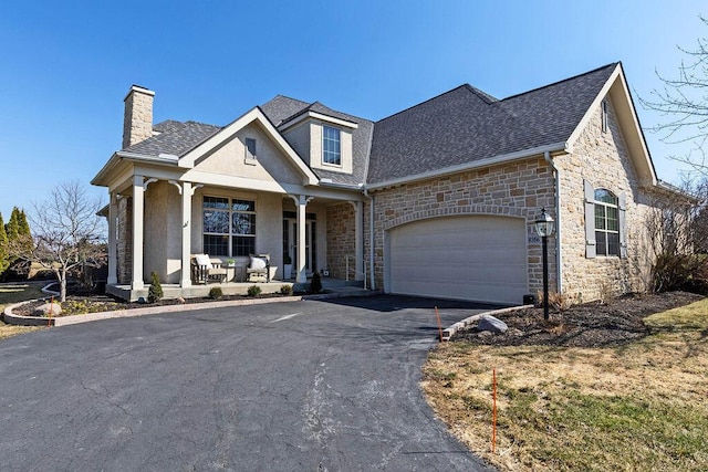 view of front of house with driveway, an attached garage, covered porch, a chimney, and stone siding