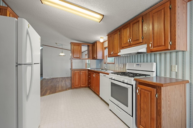 kitchen featuring under cabinet range hood, white appliances, and brown cabinets