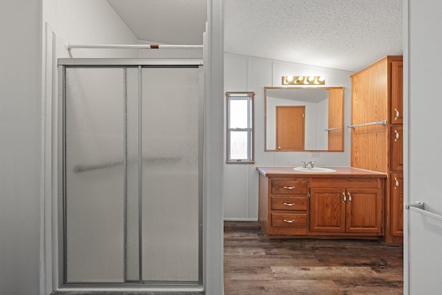 bathroom featuring a shower stall, vanity, vaulted ceiling, wood finished floors, and a textured ceiling