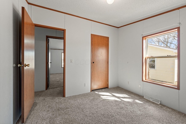 unfurnished bedroom featuring visible vents, a textured ceiling, crown molding, and carpet floors