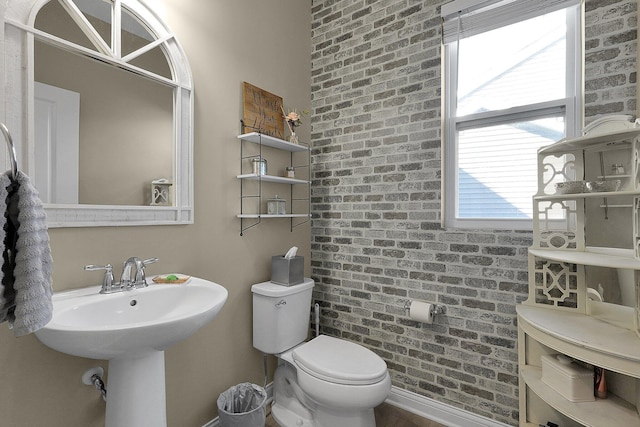 bathroom featuring toilet and brick wall