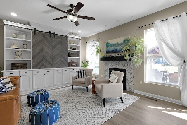 sitting room with visible vents, baseboards, light wood-type flooring, a fireplace, and a ceiling fan