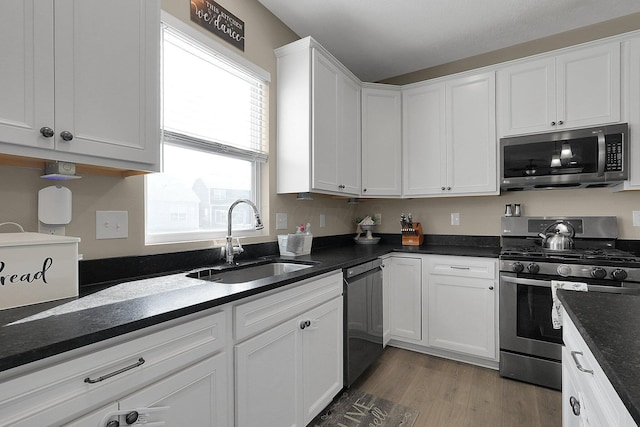 kitchen featuring dark stone counters, light wood-style flooring, a sink, stainless steel appliances, and white cabinets